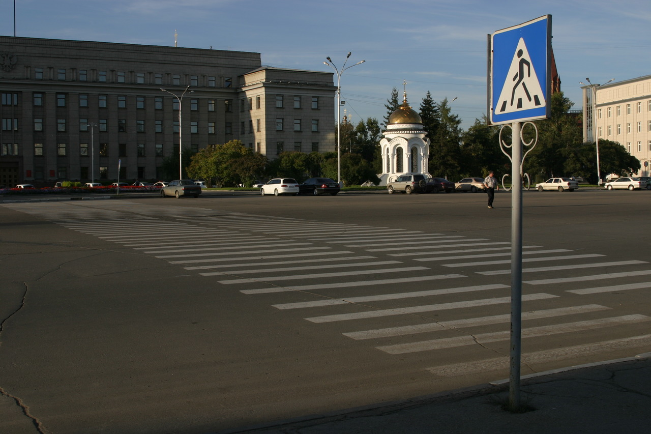 Вид на здание Правительства Иркутской области с пешеходным переходом и часовней на фоне.
