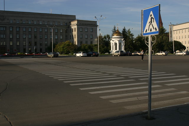 Вид на здание Правительства Иркутской области с пешеходным переходом и часовней на фоне.