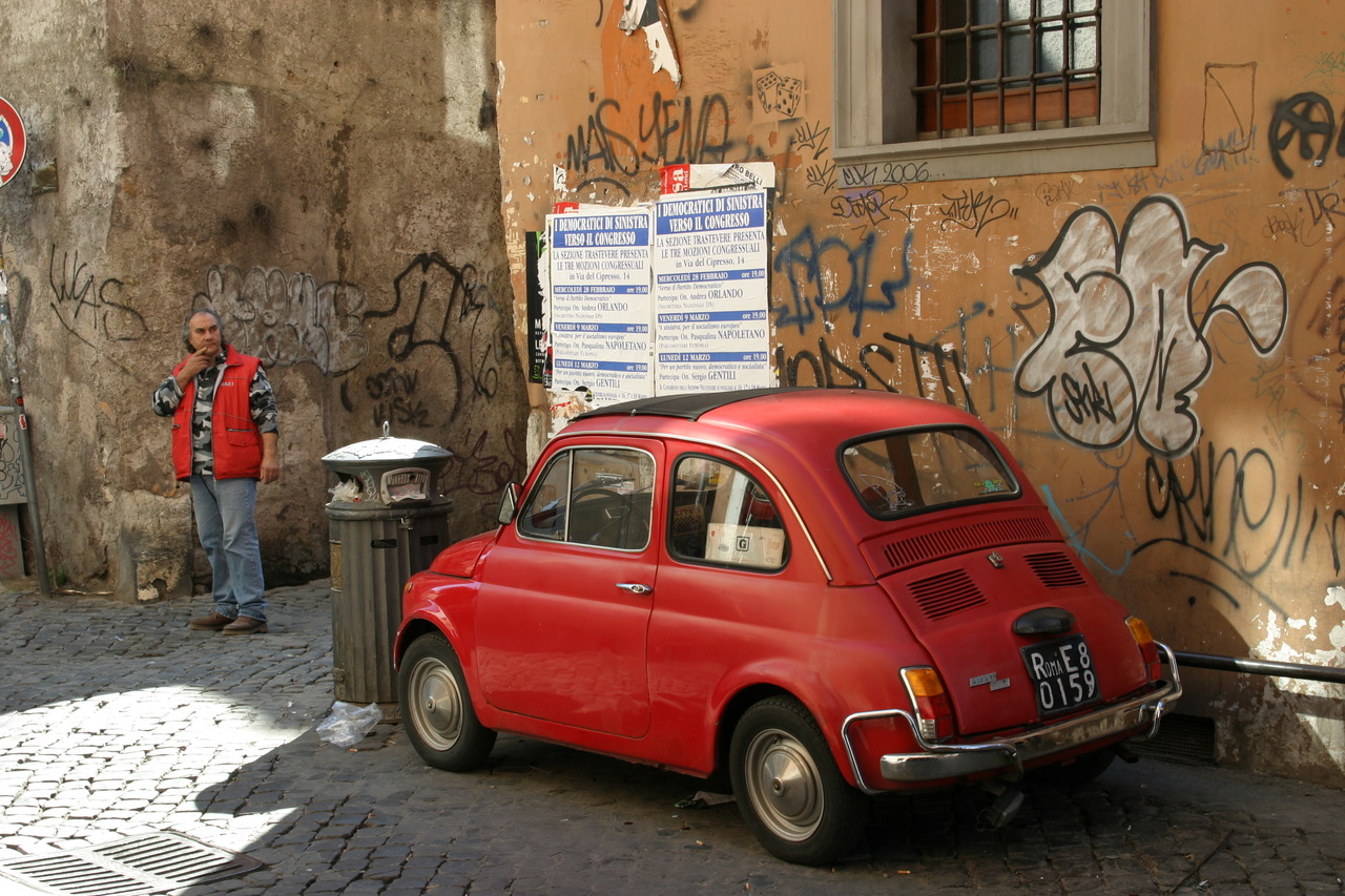 Красный автомобиль Fiat 500 на фоне стены с граффити в Риме