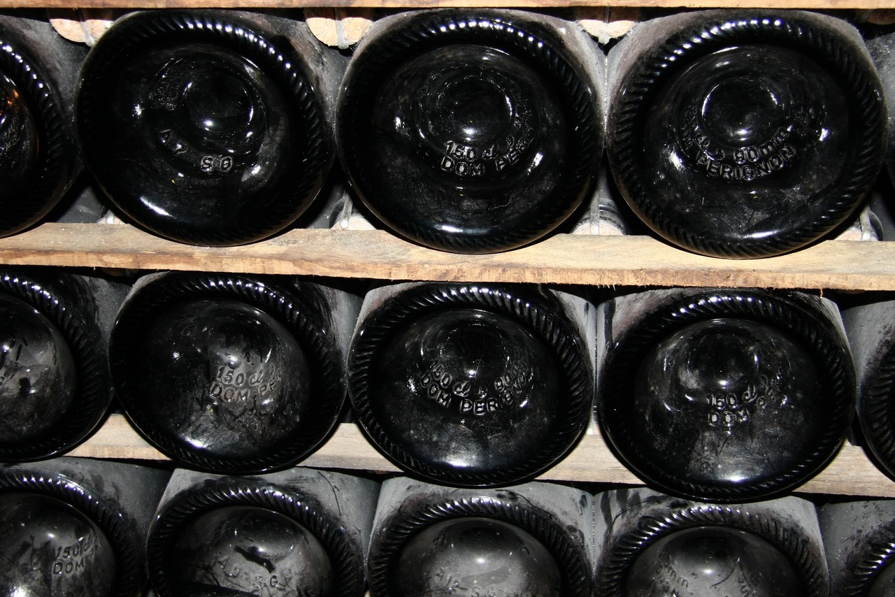 Ряды темных бутылок шампанского Dom Pérignon, сложенных в деревянный стеллаж, видны днища с гравировкой.