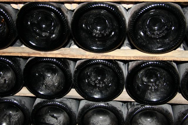 Ряды темных бутылок шампанского Dom Pérignon, сложенных в деревянный стеллаж, видны днища с гравировкой.