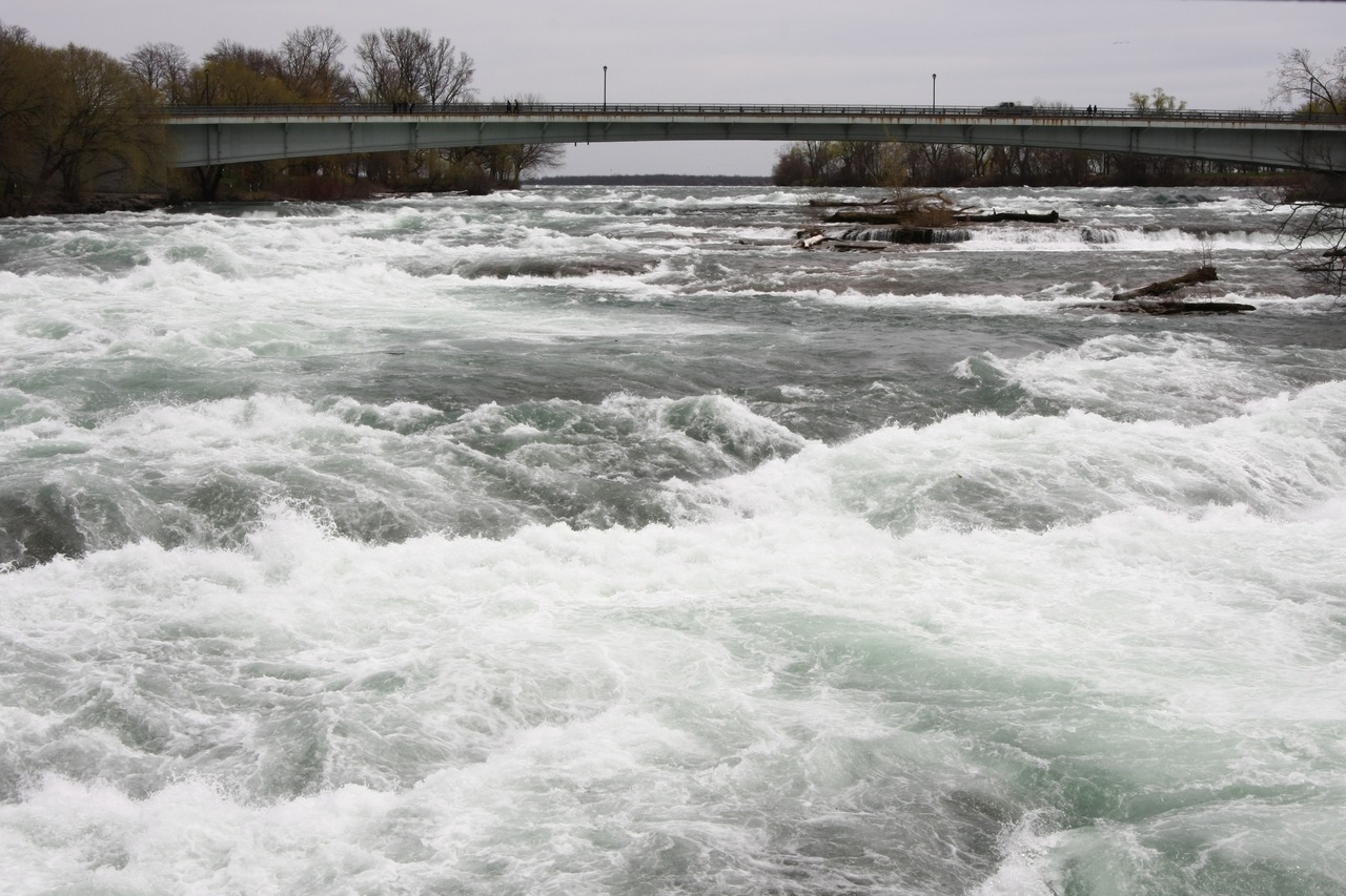 Бурная река Ниагара с белыми водоворотами и мостом на заднем плане