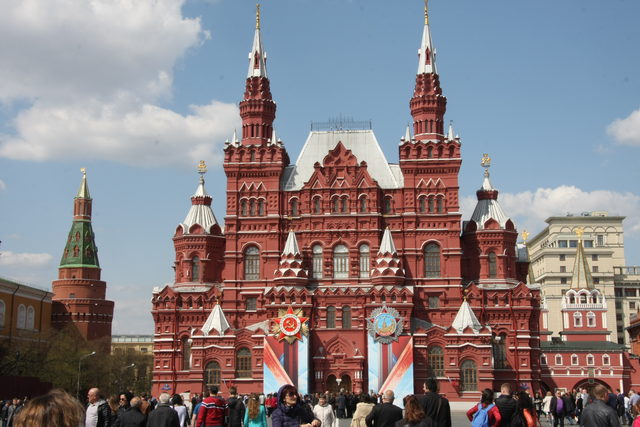 Красное здание Государственного исторического музея с баннерами и людьми на фоне голубого неба