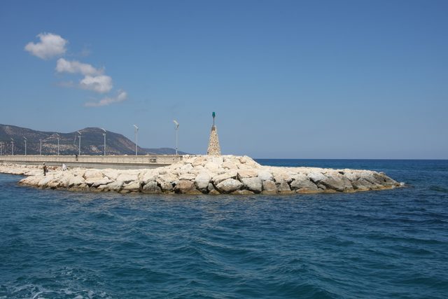 Каменный волнорез с маяком в гавани Лачи на фоне моря и гор