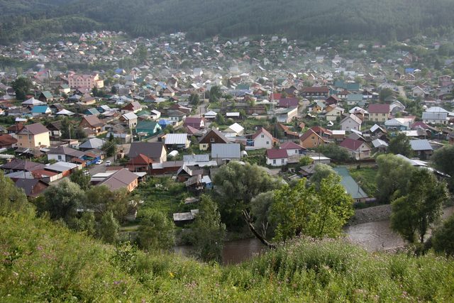 Вид на село Солонешное в долине с зелеными холмами и рекой на переднем плане