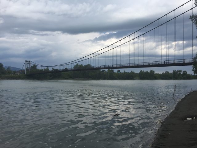 Вид на длинный подвесной мост через широкую реку Катунь с берега.